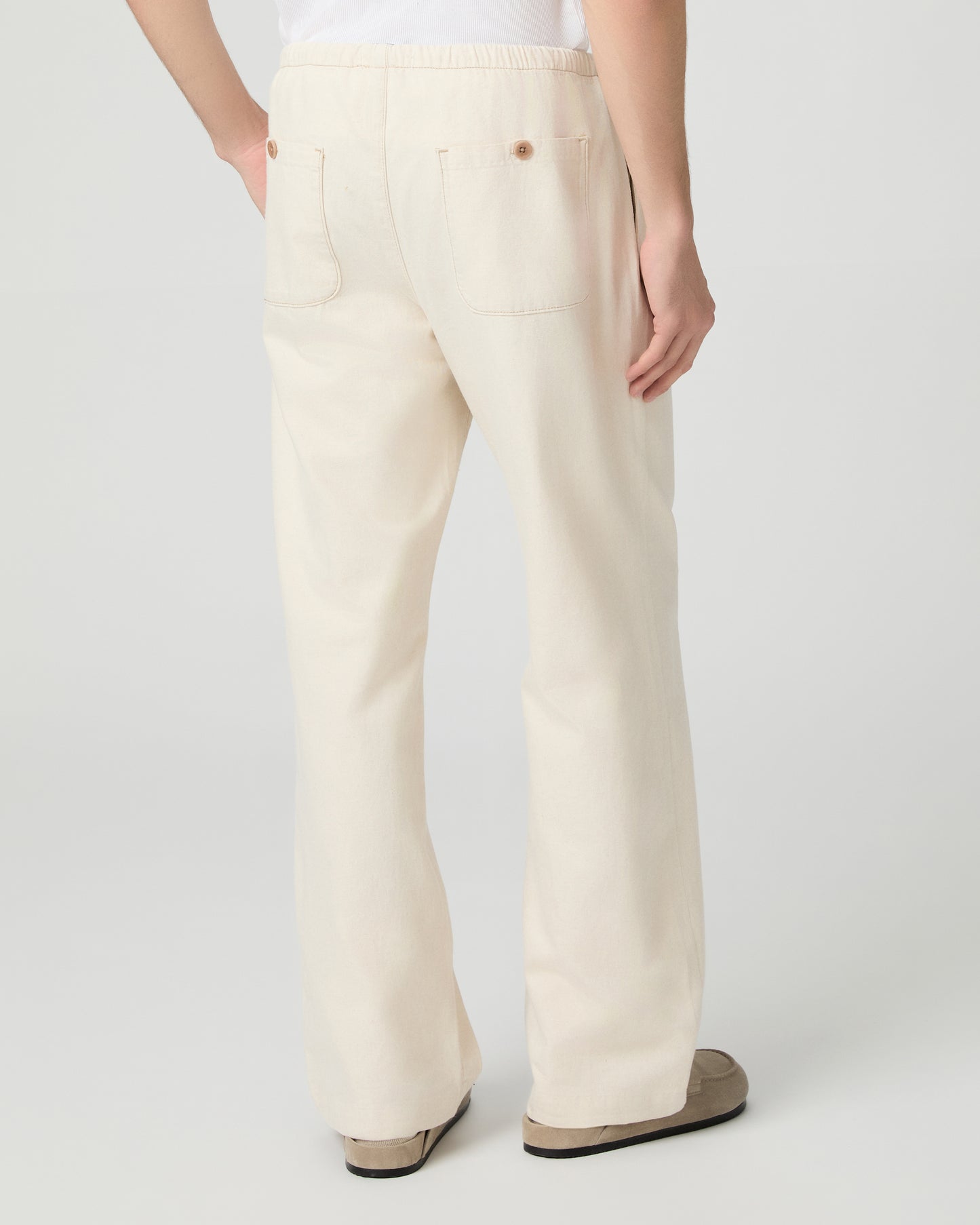 Man wearing a white tee and beige linen pants paired with grey shoes on a white background