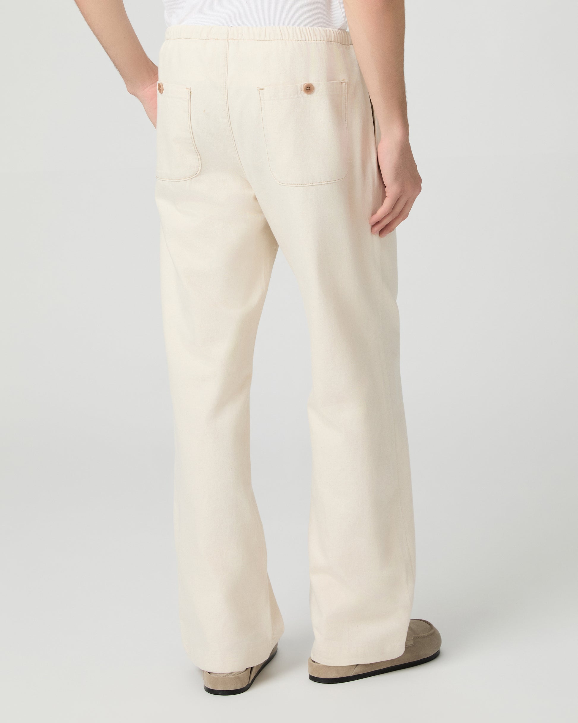 Man wearing a white tee and beige linen pants paired with grey shoes on a white background