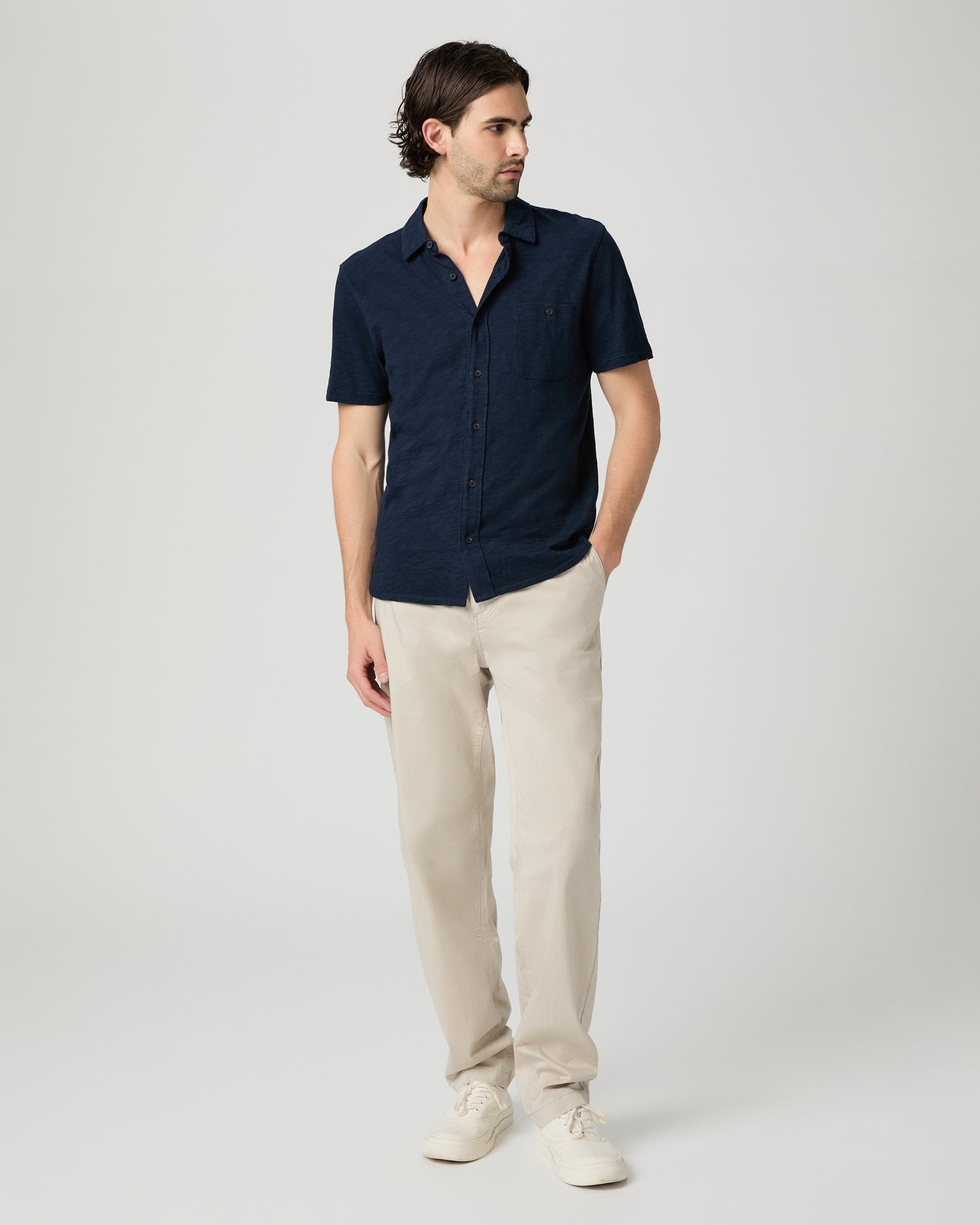Man wearing a navy shirt and beige pants on a white background