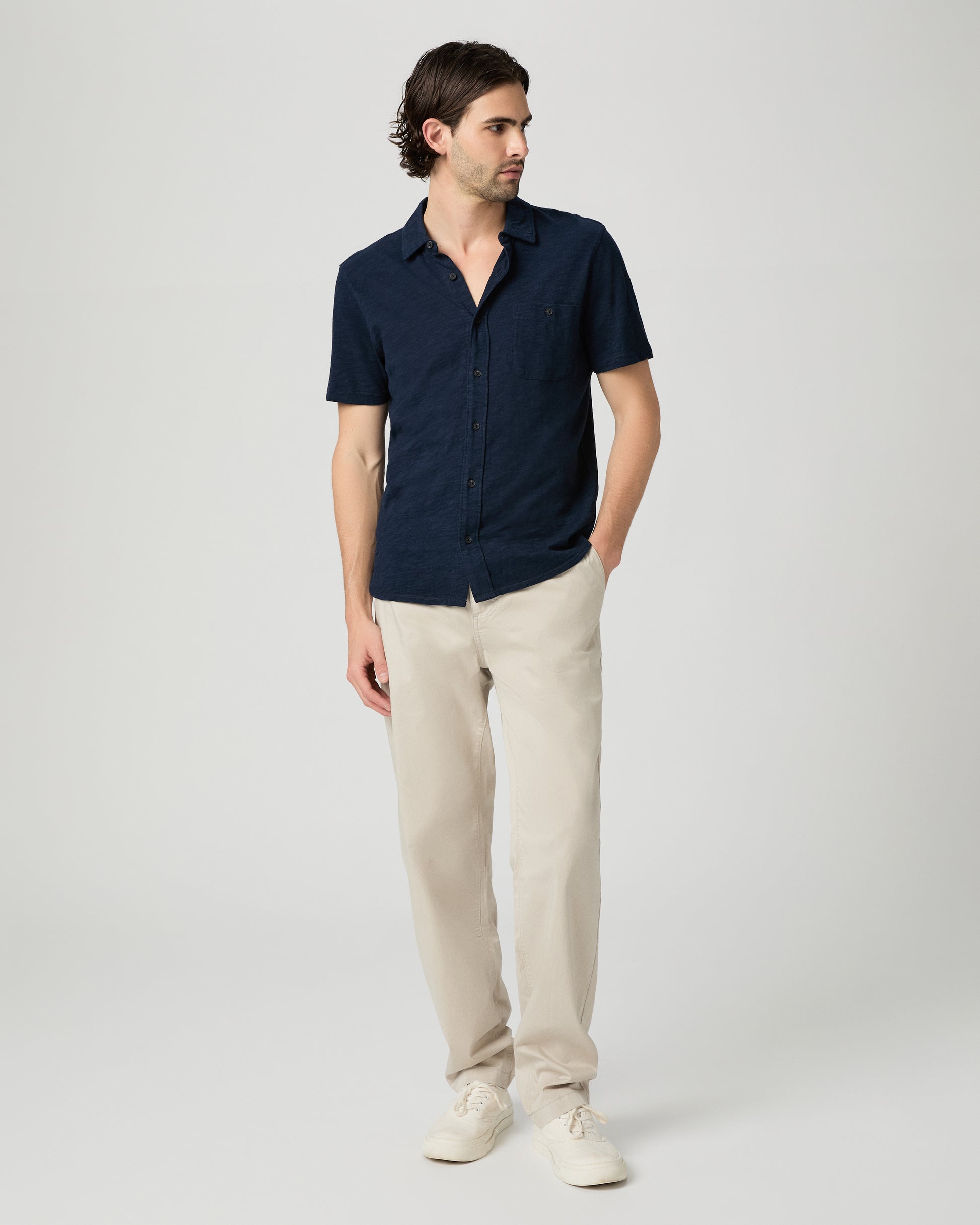 Man wearing a navy shirt and beige pants on a white background