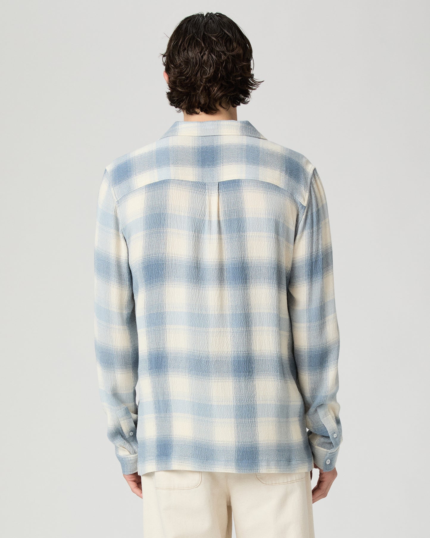 Man wearing a blue and white checkered shirt against a plain background