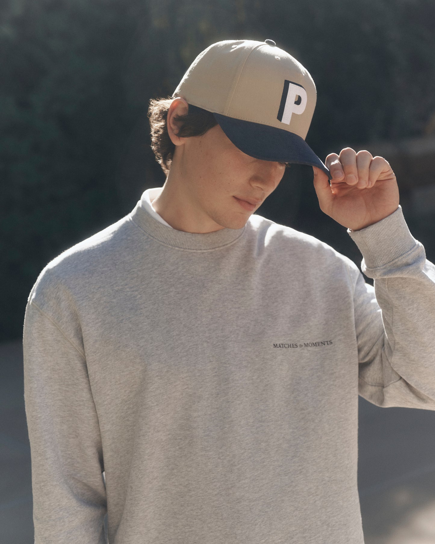 Person wearing a beige cap with a logo and a gray sweatshirt outdoors