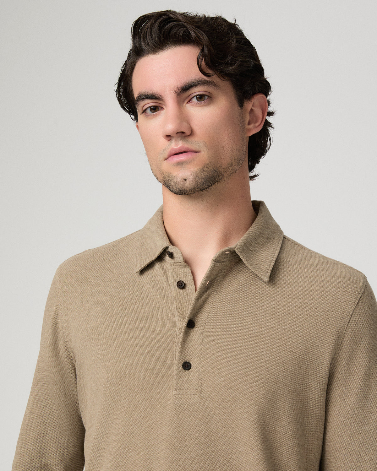 Man wearing beige top and brown pants against a white background