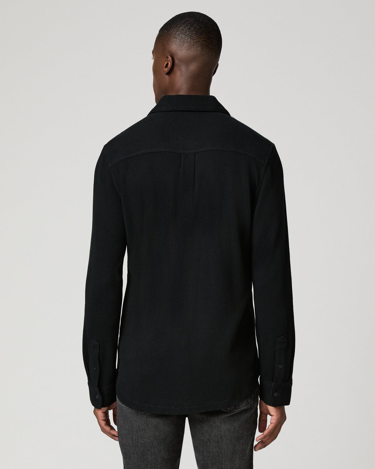Close-up back view of a man wearing the black waffle-knit shirt, showing the back yoke seam and textured knit fabric.