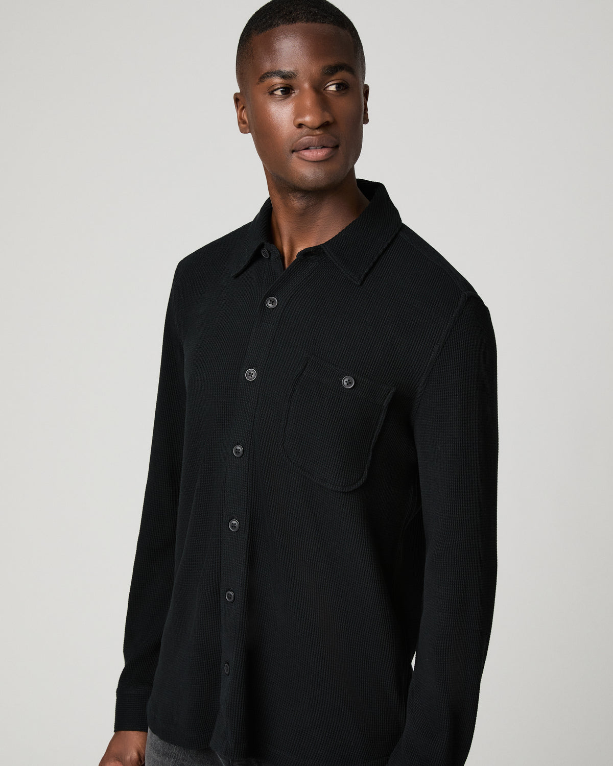 Close-up front view of a man in a black waffle-knit shirt, highlighting the chest pocket and textured fabric detail.