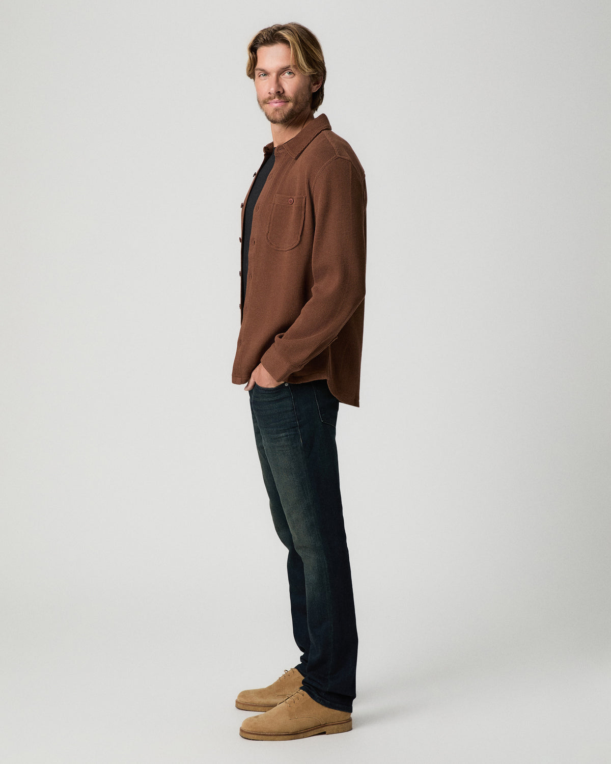 Side profile of model with one hand in his pocket, wearing the Hollander Shirt in Sepia Clay with dark-wash jeans and tan suede boots