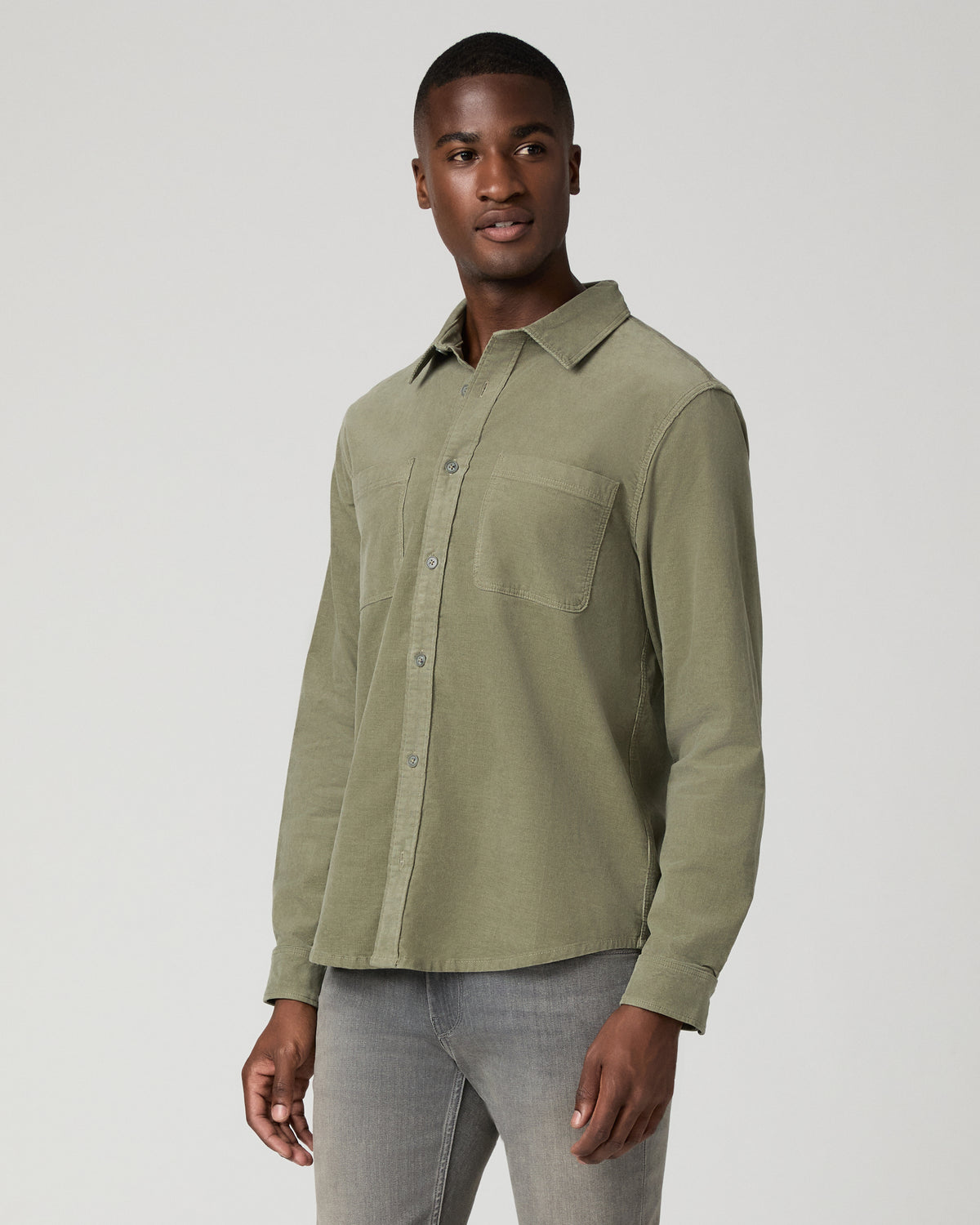 Three-quarter side view of a man in a sage green corduroy shirt, highlighting the chest pocket and button placket against gray jeans.