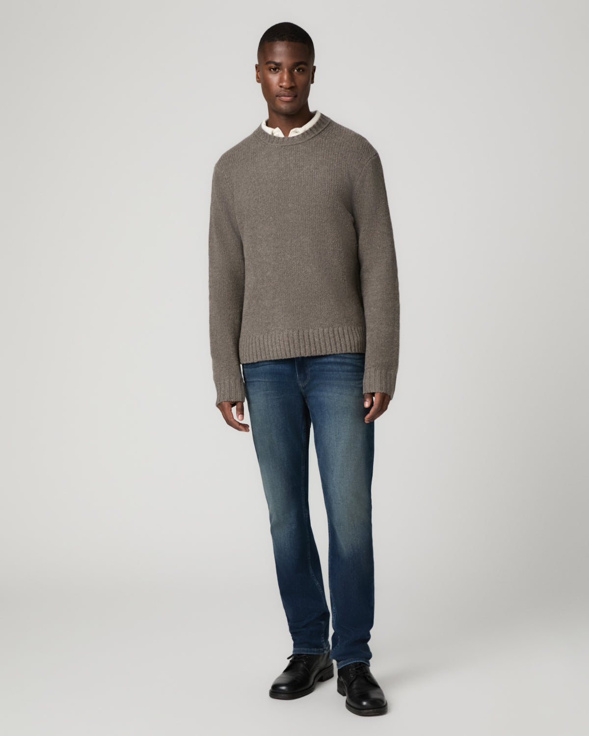 Full-length front view of a man wearing the dark heather grey crewneck sweater over a white collared shirt with dark wash jeans and black shoes, standing with arms at his sides.