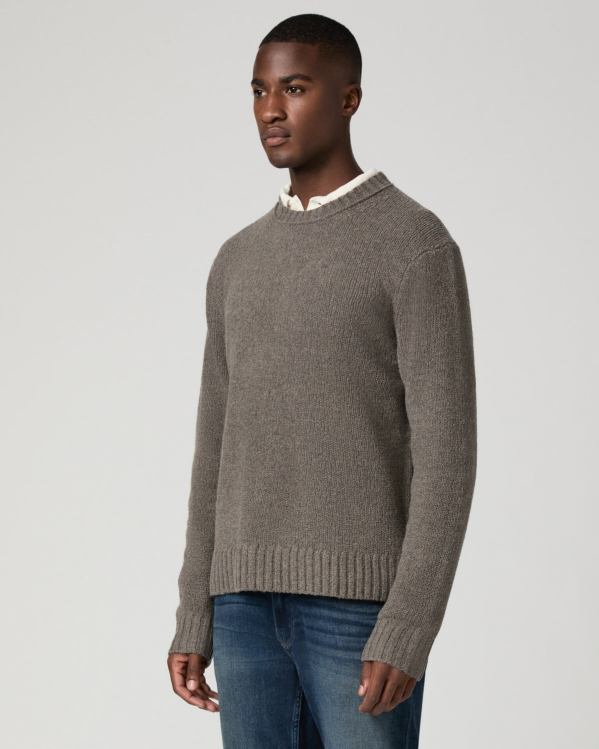 Three-quarter view of a man wearing the dark heather grey crewneck sweater over a white collared shirt, looking off to the side, paired with dark wash jeans.
