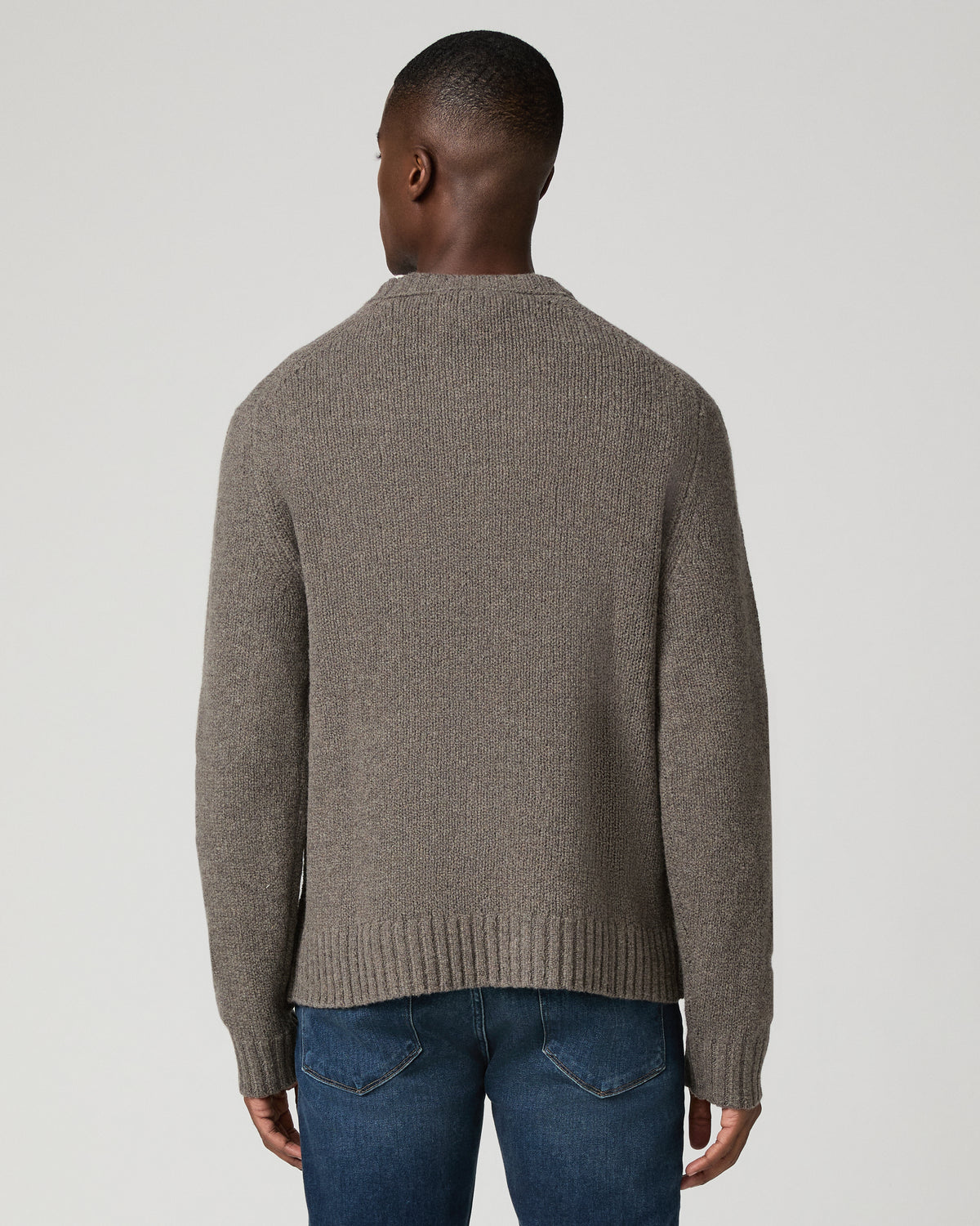 Back view of a man wearing the dark heather grey crewneck sweater, showing the ribbed knit texture and straight hem, paired with dark wash jeans.