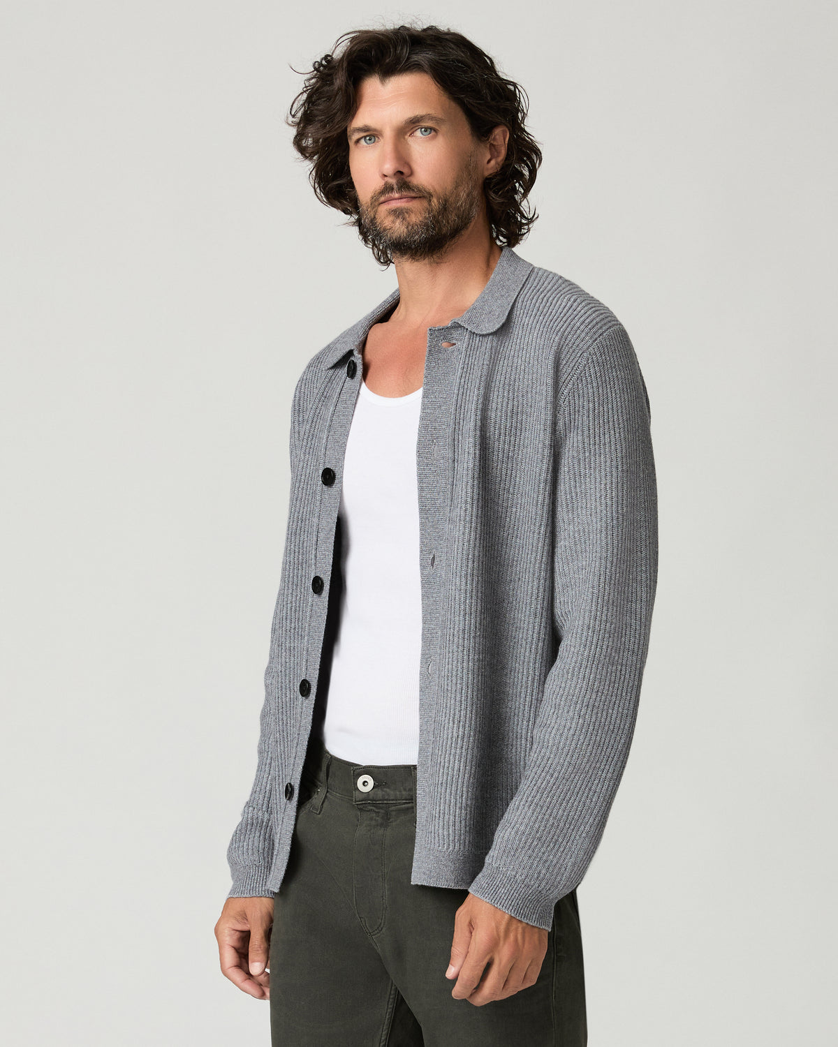 Three-quarter angle view of a man wearing the heather gray ribbed-knit Spokane Cardigan open over a white tank top, one hand resting near his pocket, paired with dark olive trousers.