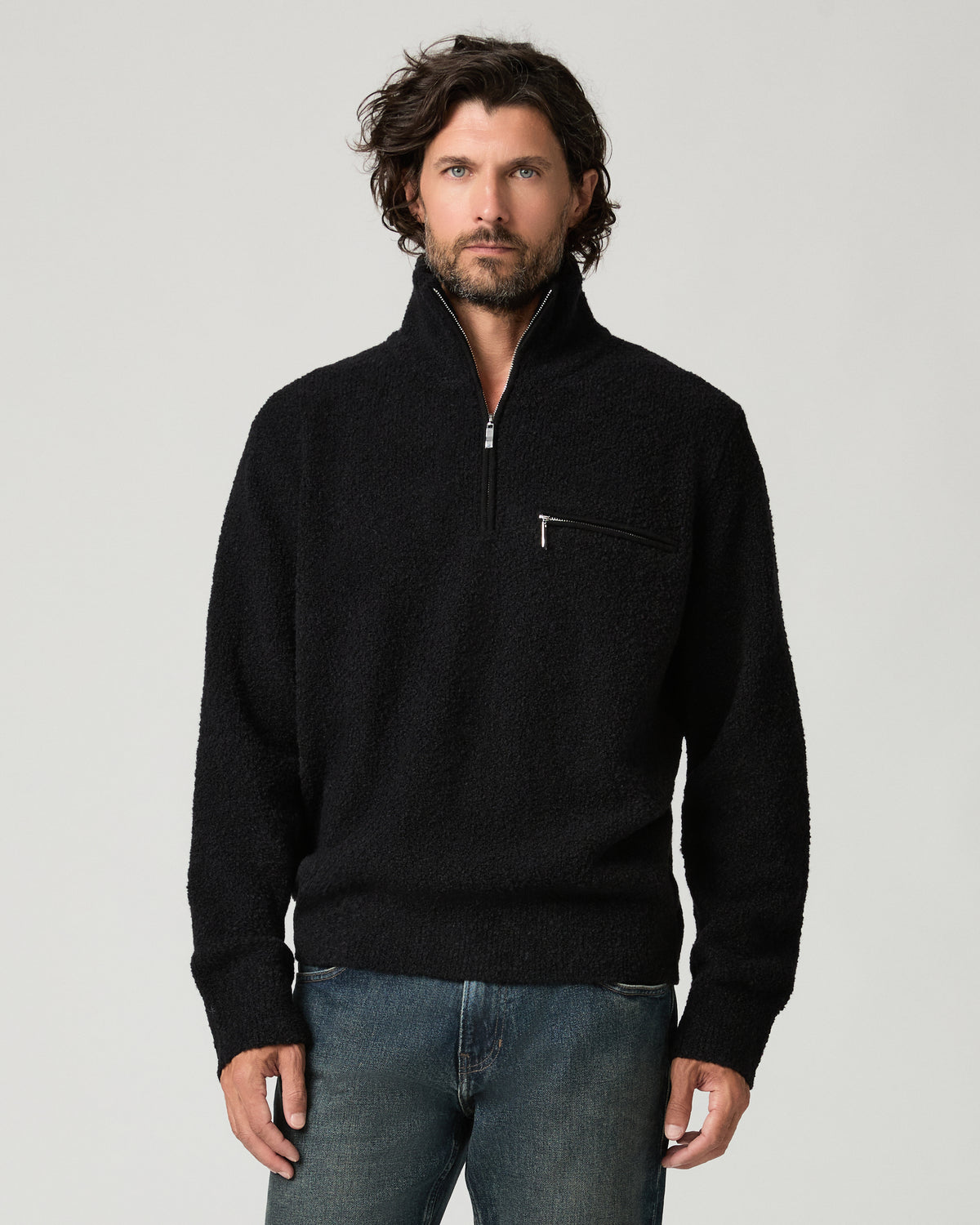 Front view of a man wearing the black bouclé-knit Donover Quarter Zip Sweater with a half-zipped funnel collar and zip chest pocket, paired with faded blue jeans.