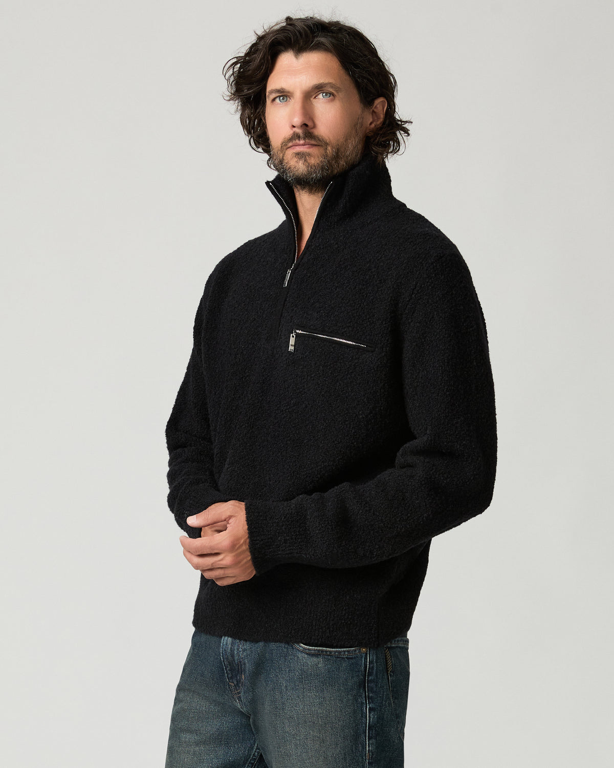 Cropped three-quarter view of a man adjusting the zipper pull on the black bouclé-knit Donover Quarter Zip Sweater, showing the ribbed cuffs and hem.