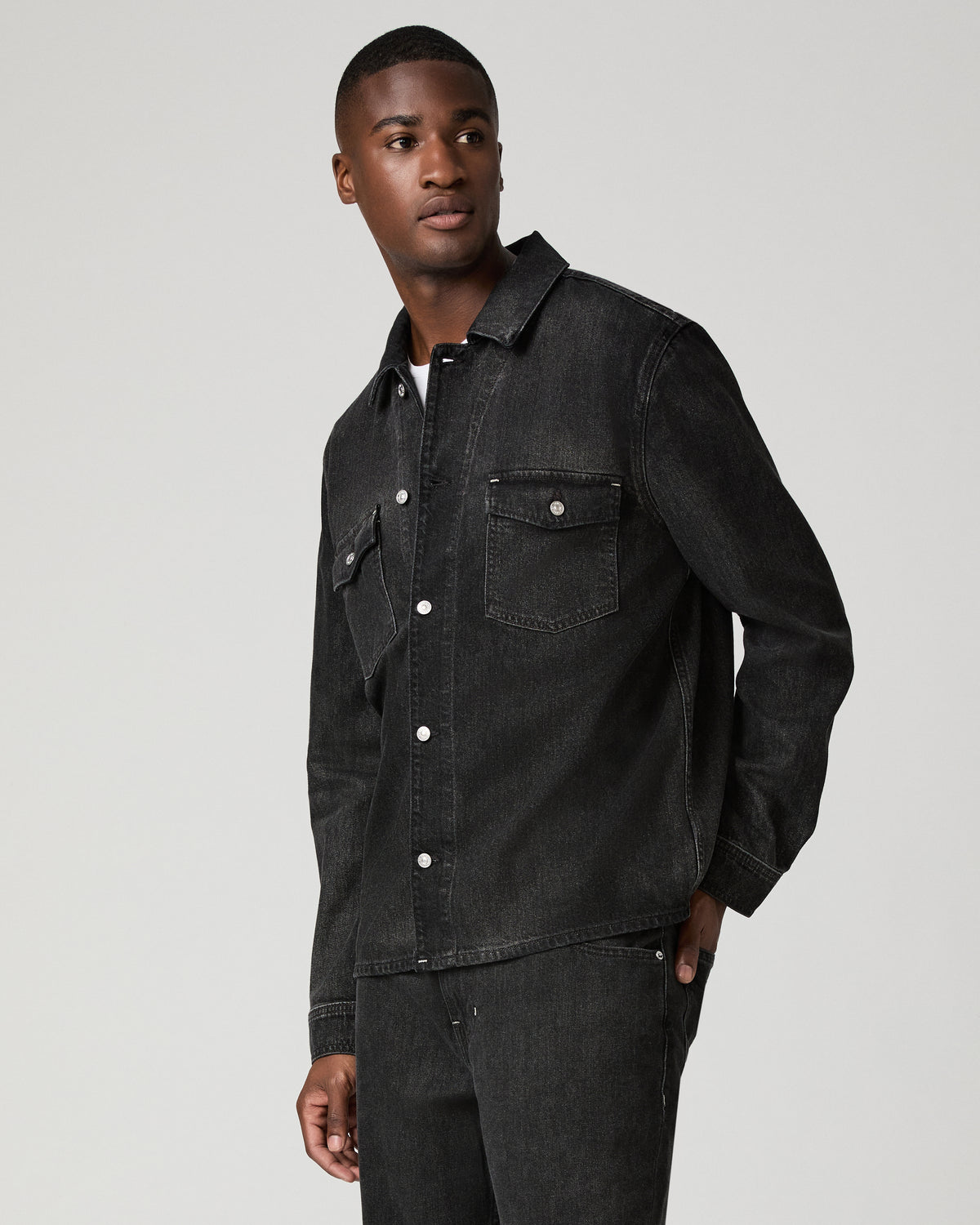 Three-quarter side view of a man in a charcoal denim shirt, highlighting the snap-button placket and chest pocket detail.