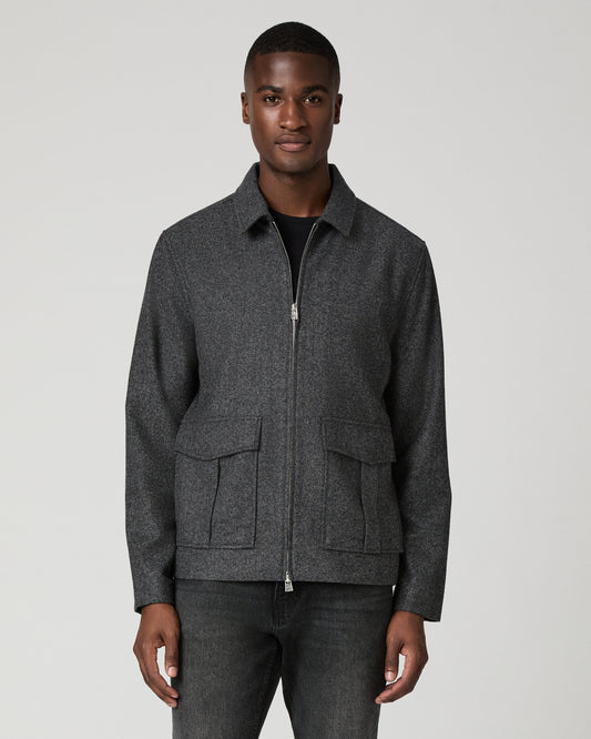 Front view of a man wearing the charcoal brushed-wool Dilworth Jacket fully zipped with utility-inspired flap patch pockets, over a black tee and dark gray jeans.