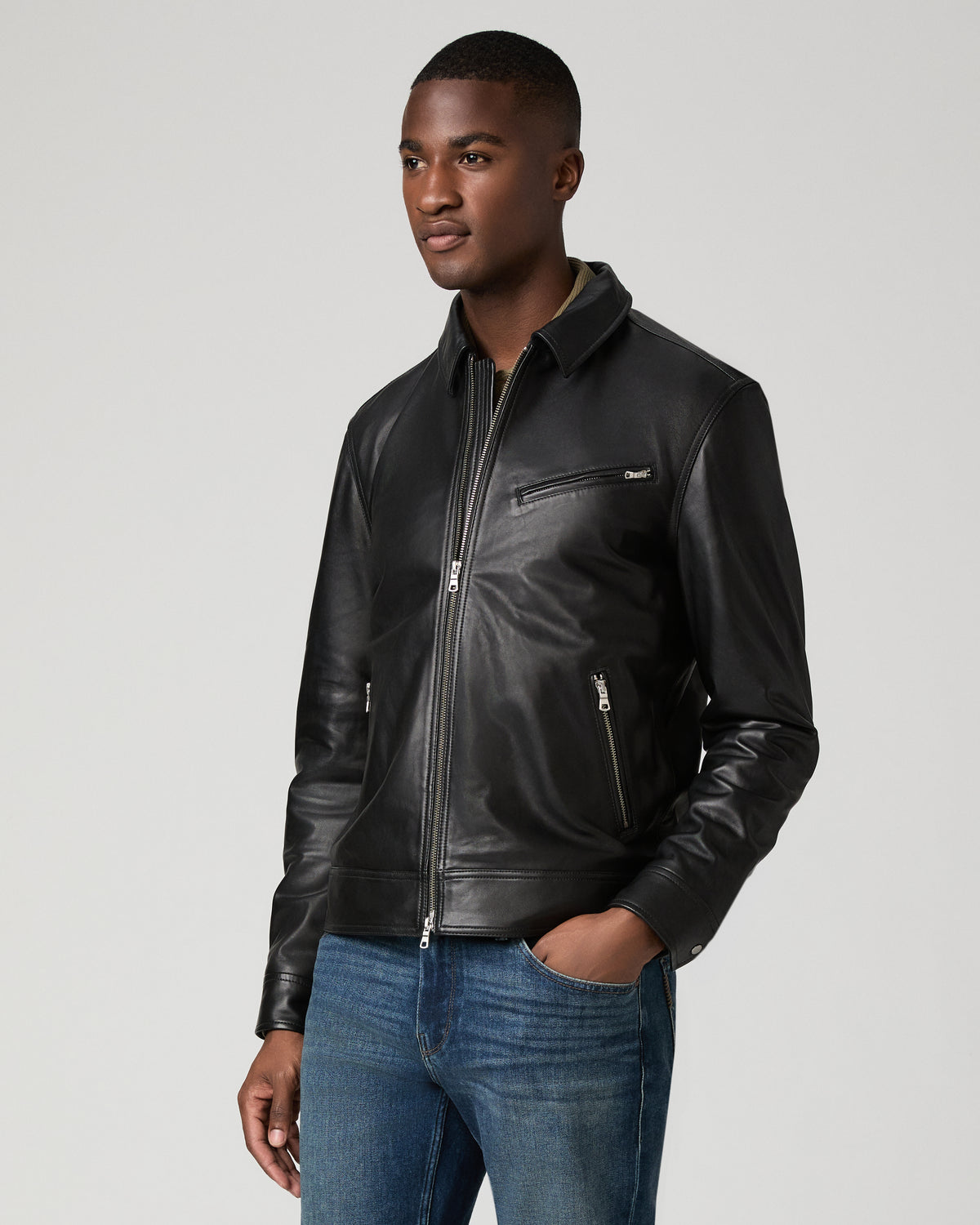 Three-quarter angle view of a man wearing the black leather Rocoso Moto Jacket fully zipped, hand in his jean pocket, showing the zip chest and hip pockets.
