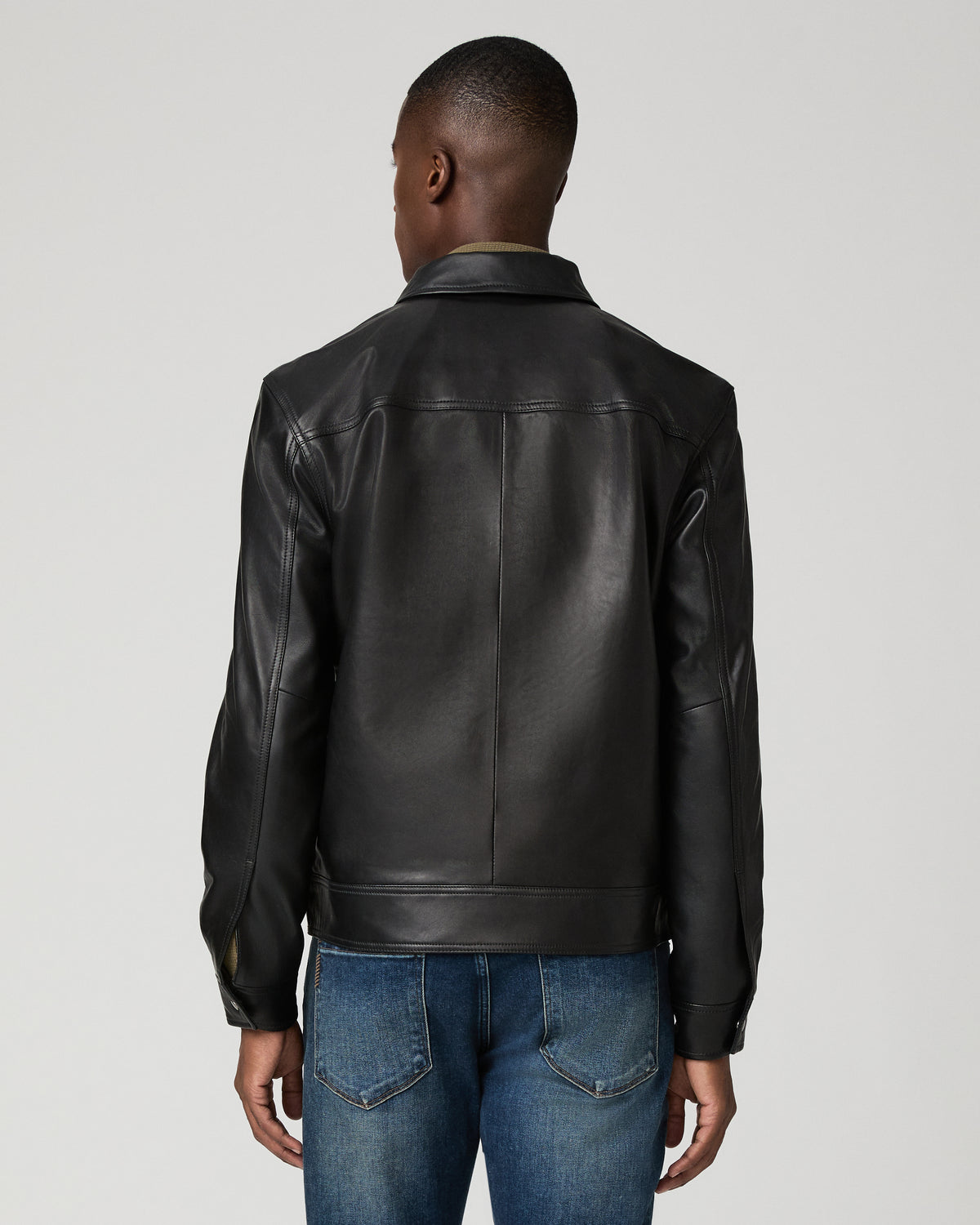 Back view of a man wearing the black leather Rocoso Moto Jacket, highlighting the seam detailing across the shoulders and back paired with blue jeans.