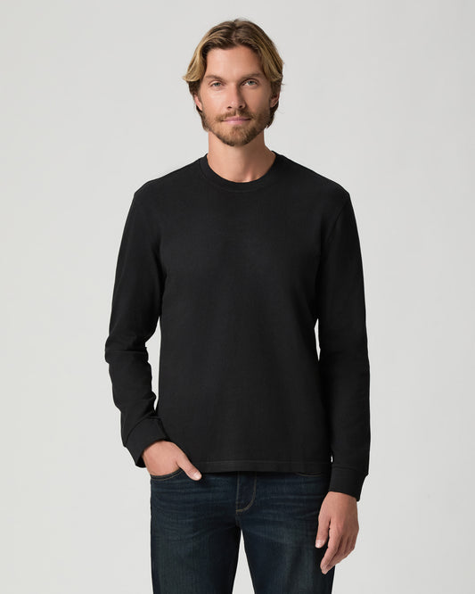 Model standing with one hand in his pocket, wearing the Norcross Long Sleeve Boxy Tee in Vintage Black with dark-wash jeans