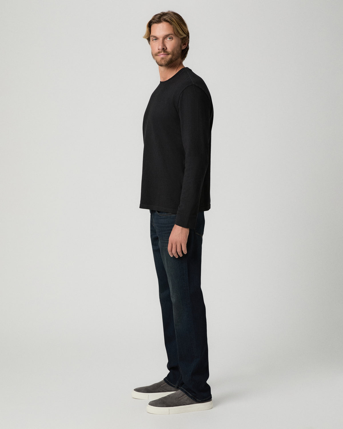 Side profile of model wearing the Norcross Long Sleeve Boxy Tee in Vintage Black with dark-wash jeans and grey slip-on shoes
