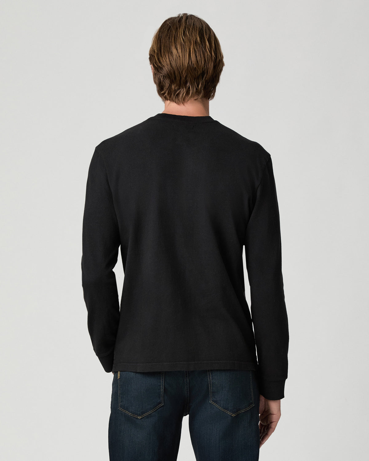 Back view of model wearing the Norcross Long Sleeve Boxy Tee in Vintage Black with dark-wash jeans