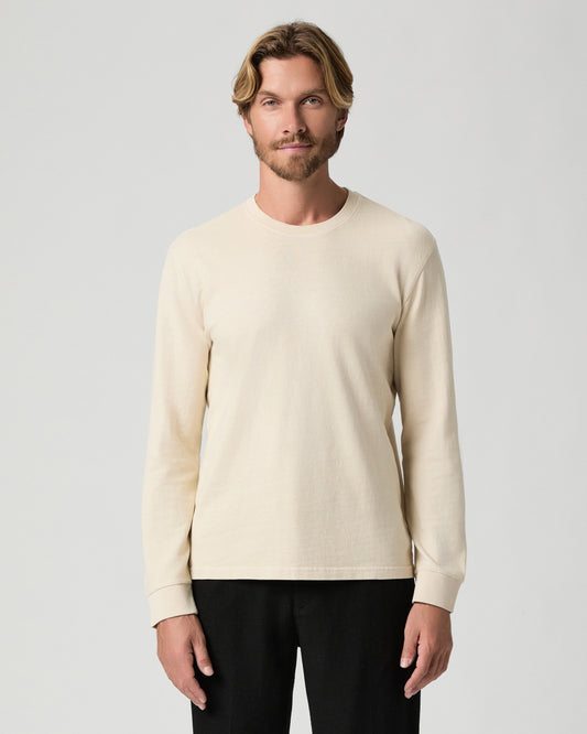 Model standing with arms at his sides, wearing the Norcross Long Sleeve Boxy Tee in Pale Antler, a cream long-sleeve tee, with black pants