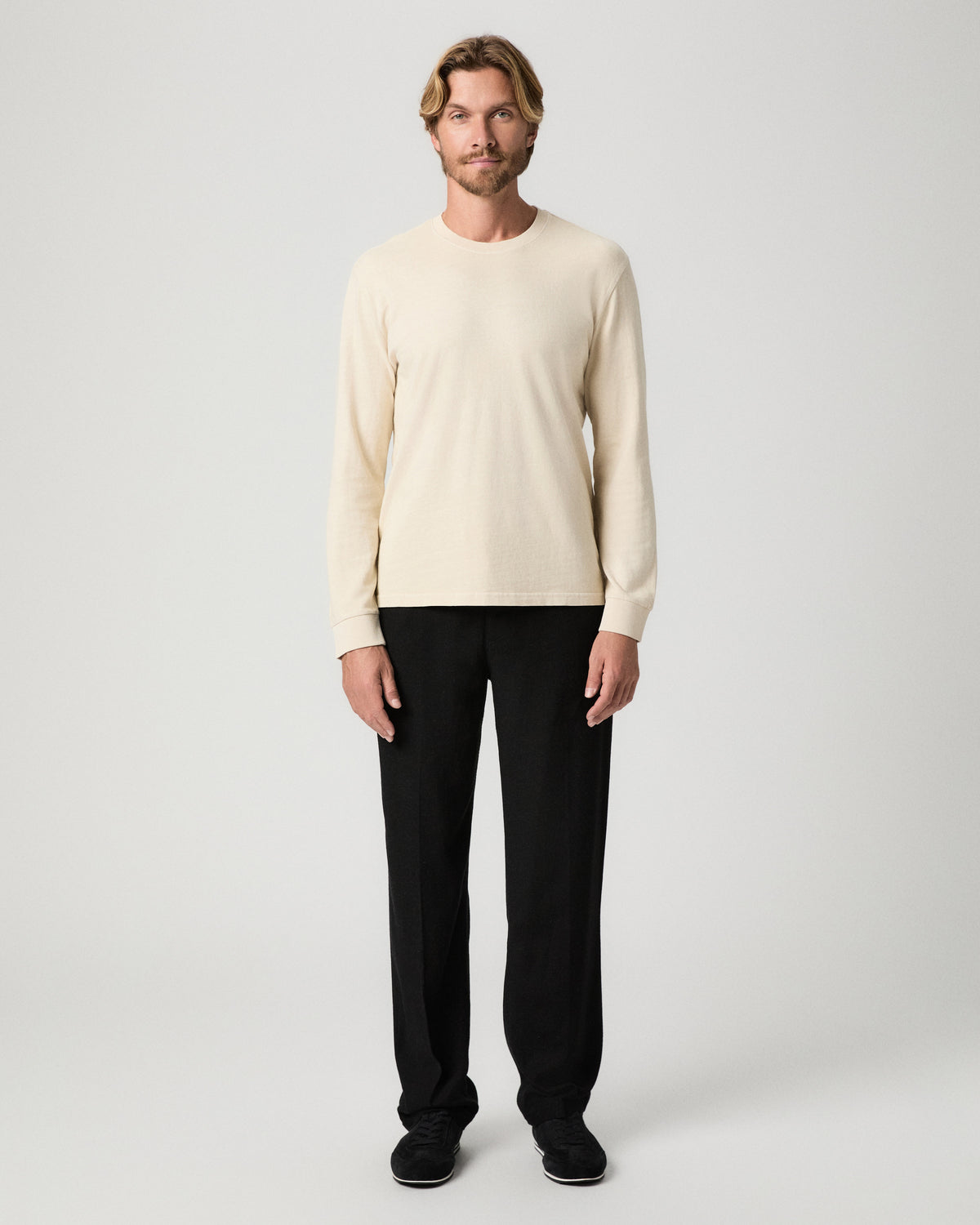 Full-length view of model standing with arms at his sides, wearing the Norcross Long Sleeve Boxy Tee in Pale Antler with black pants and black shoes