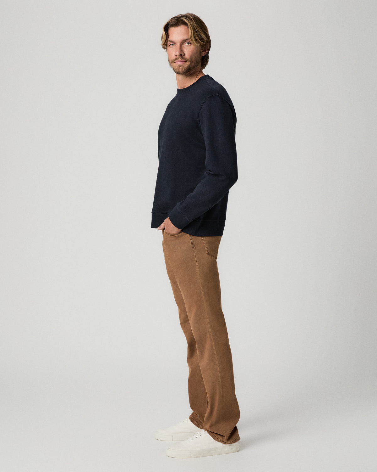 Side profile of model with one hand in his pocket, wearing the Devlin Crewneck in Deep Anchor with tan pants and white sneakers