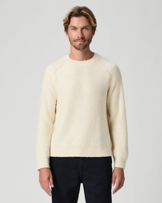 Model standing with arms at his sides, wearing the Hightower Crewneck Sweater in Marfil, a cream knit sweater, with dark jeans