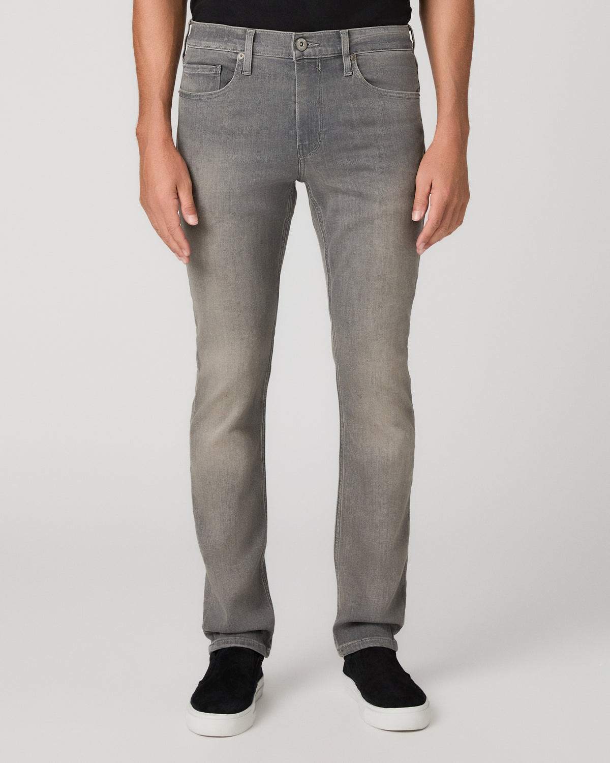 A man modeling a black short-sleeve crewneck t-shirt, light gray slim-fit jeans, and black slip-on shoes against a plain light gray studio background.