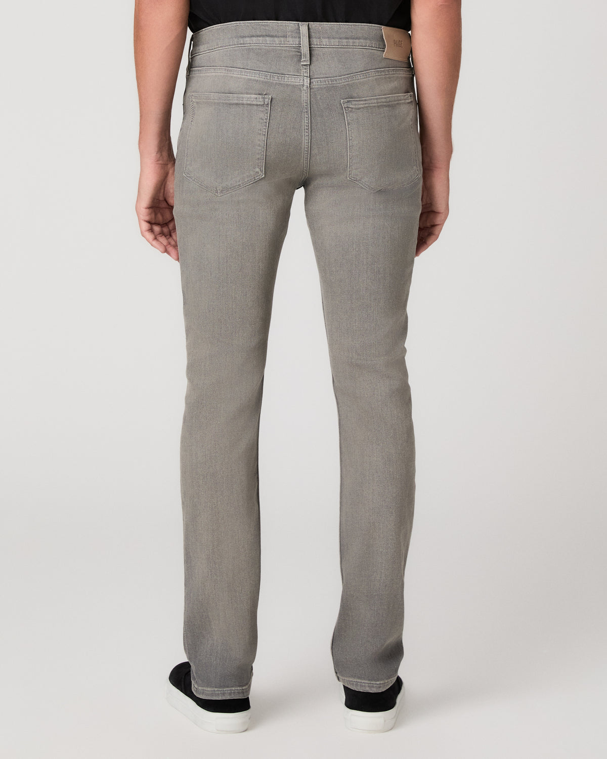 A man modeling a black short-sleeve crewneck t-shirt, light gray slim-fit jeans, and black slip-on shoes against a plain light gray studio background.