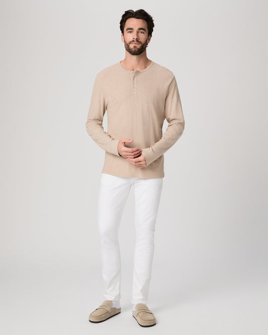 Man wearing a beige long-sleeve shirt and white pants on a plain background