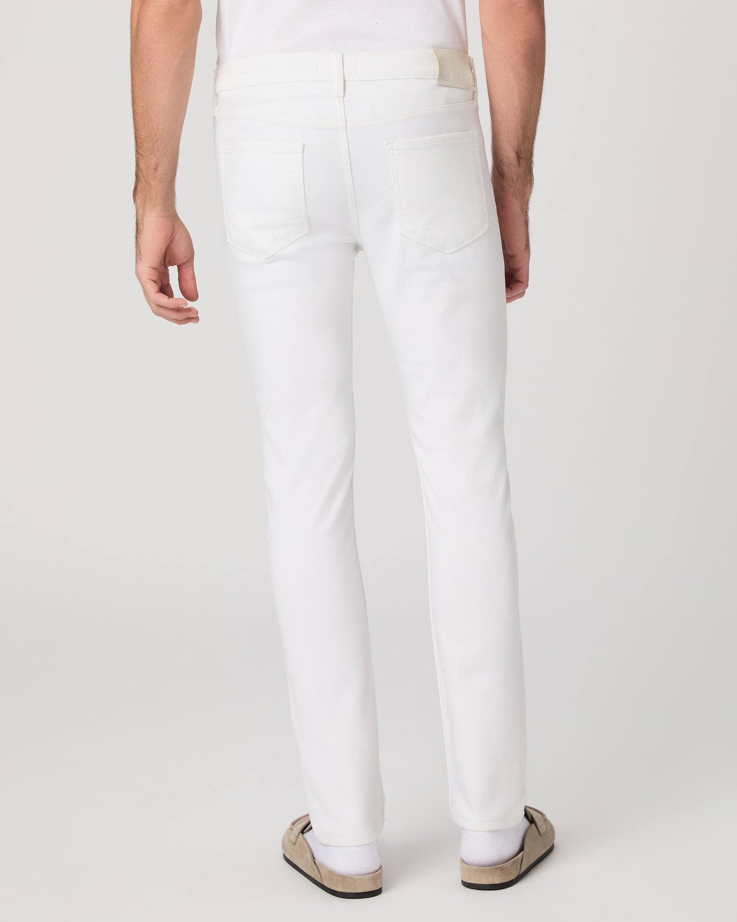 Man wearing a white shirt and white pants on a plain background