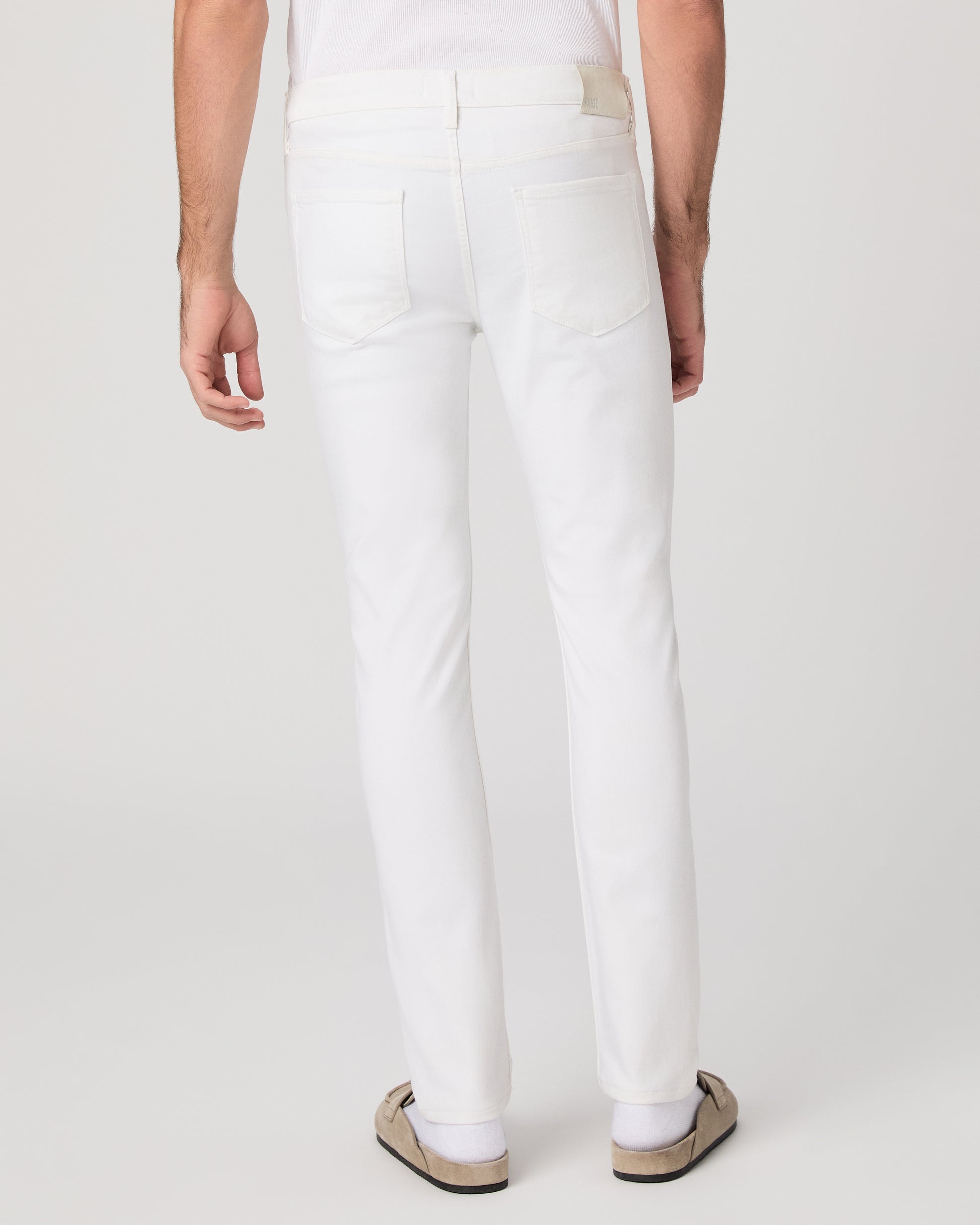 Man wearing a white shirt and white pants on a plain background