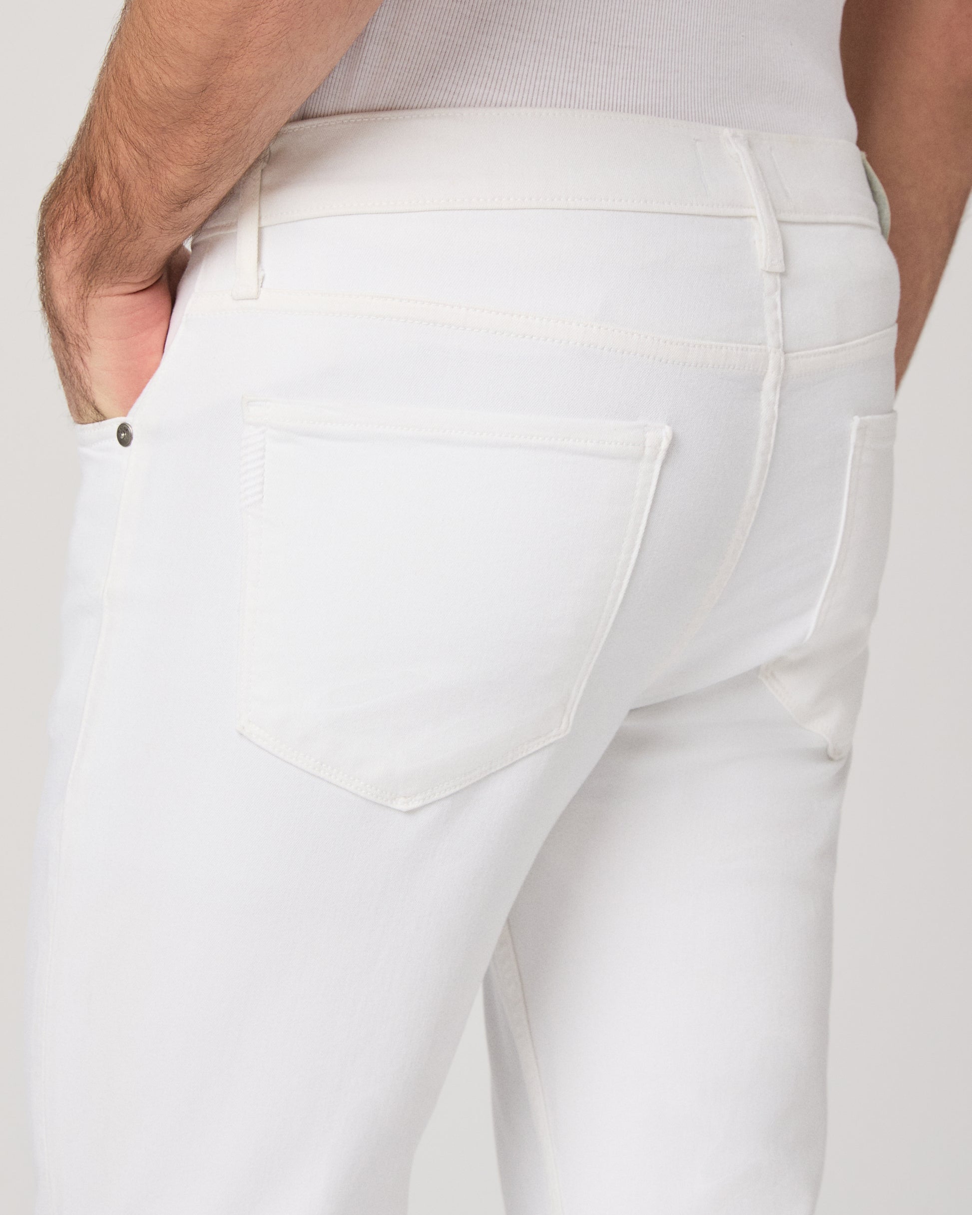Man wearing a white shirt and white pants on a plain background