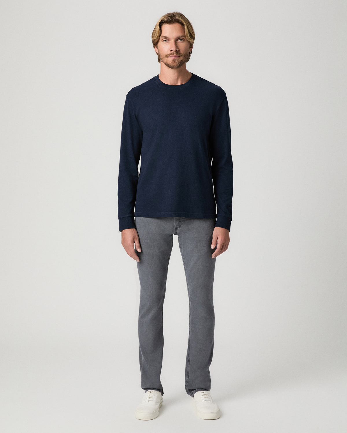 Full-length view of model standing with arms at his sides, wearing a navy long-sleeve top with the Lennox 32 Inch Slim Jean in Vintage Icy River and white sneakers