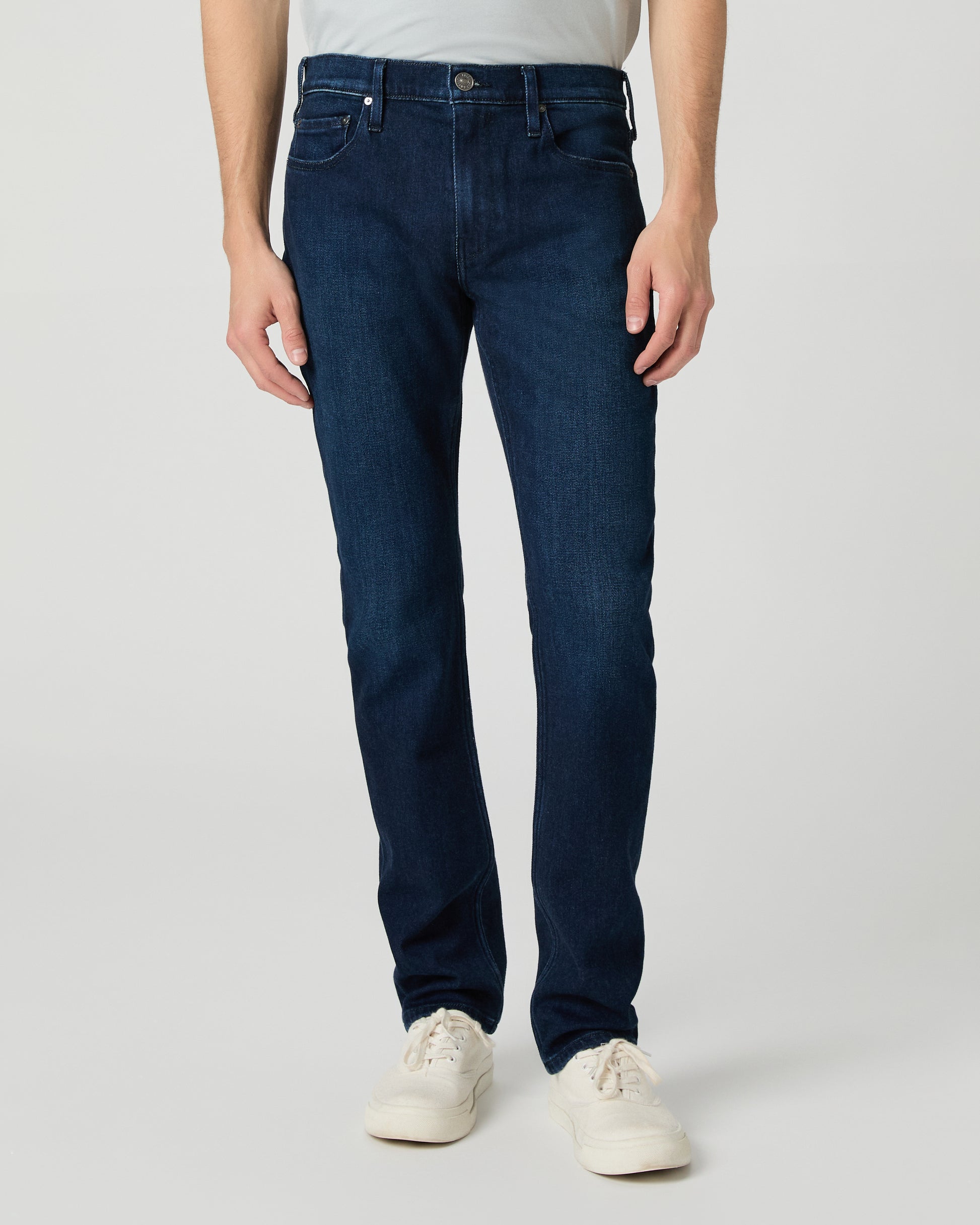 Man wearing a light gray t-shirt and dark blue jeans on a white background