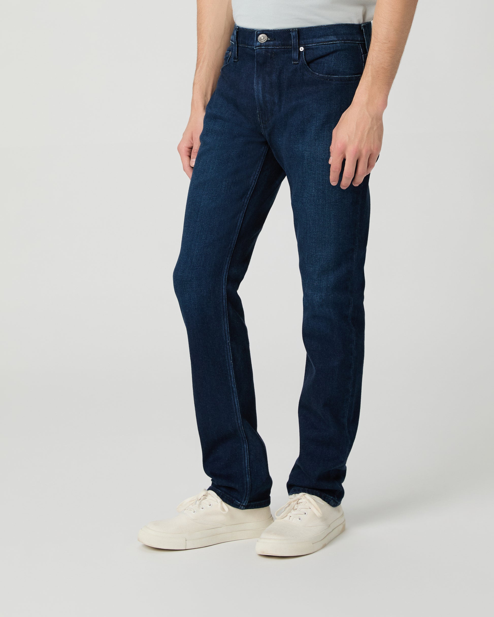 Man wearing a light gray t-shirt and dark blue jeans on a white background