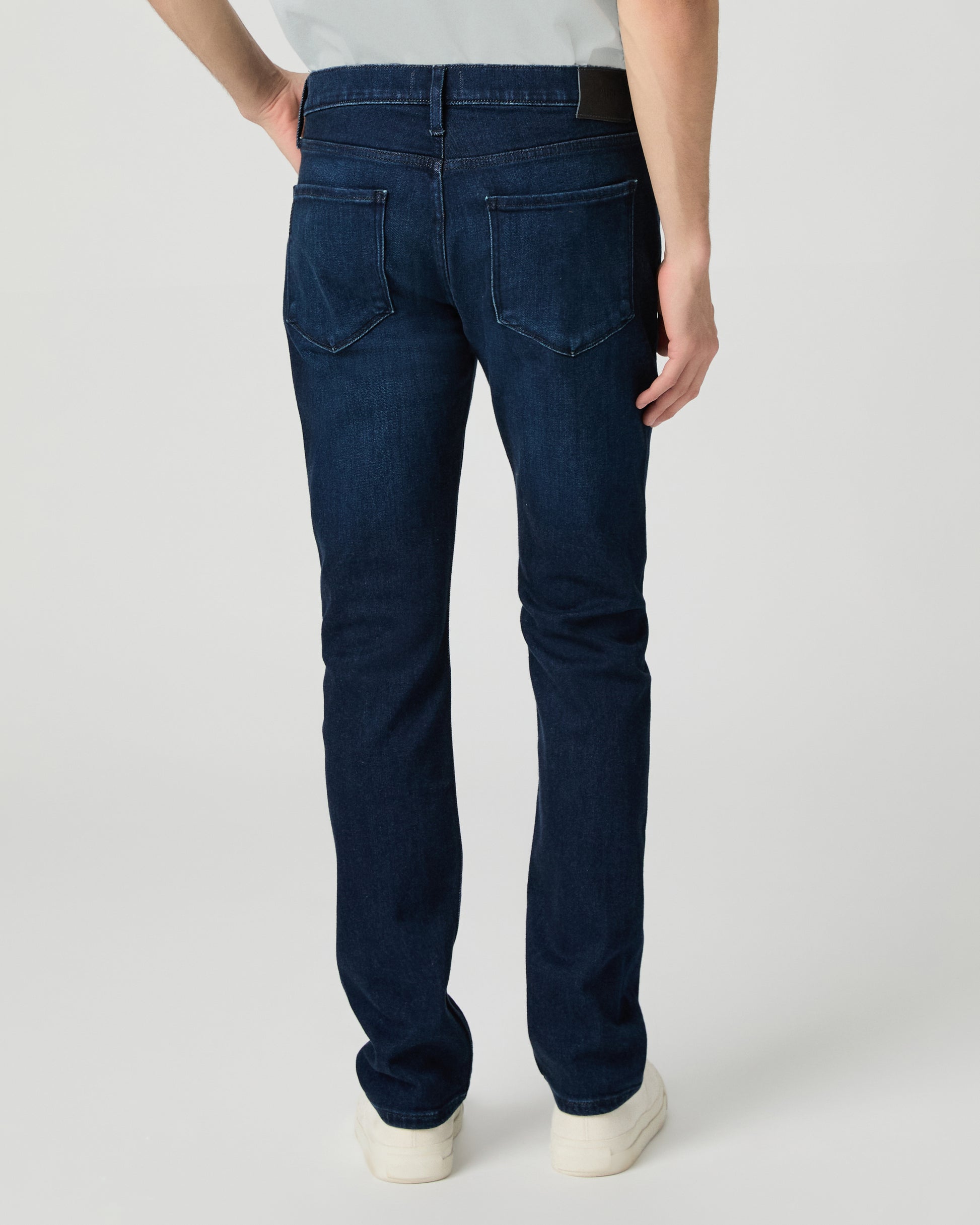 Man wearing a light gray t-shirt and dark blue jeans on a white background