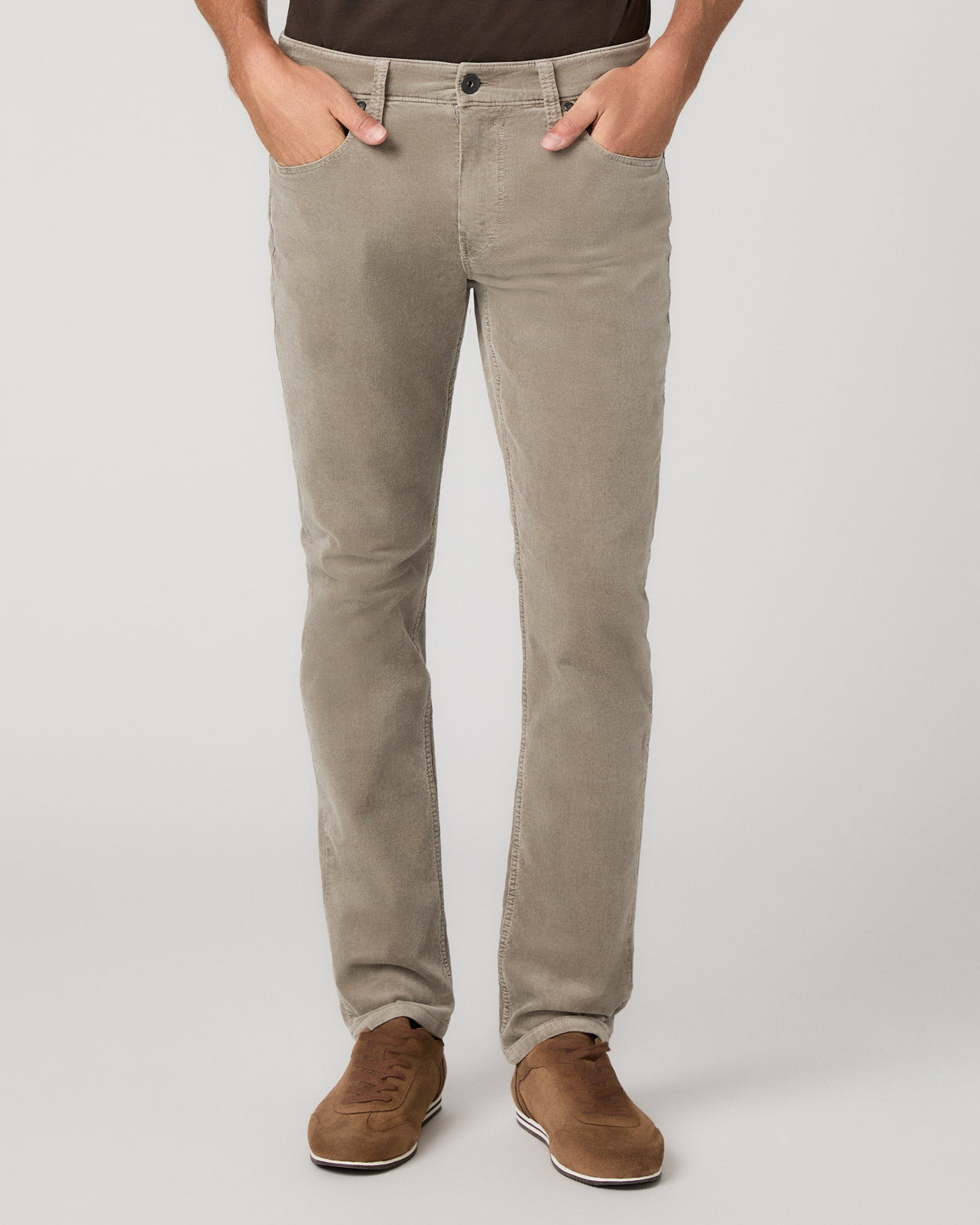 A man modeling a dark brown short-sleeve crewneck t-shirt, paired with beige trousers and brown suede shoes, standing against a light gray studio background.