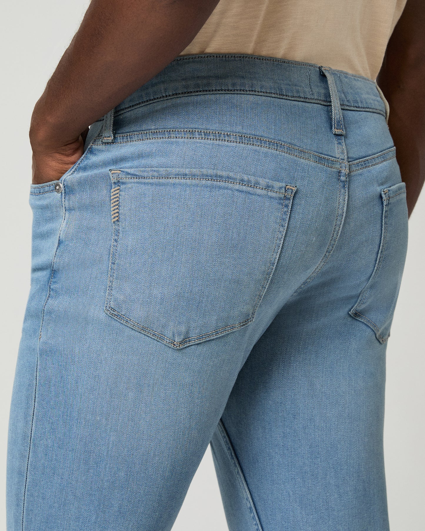 Man wearing a beige shirt and blue jeans on a white background