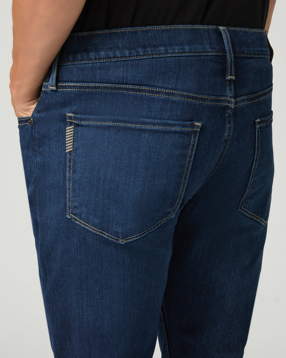 Close-up back view of deep blue slim-fit jean pockets, showing a leather brand patch, contrast stitching, and subtle whisker fading at the seat.