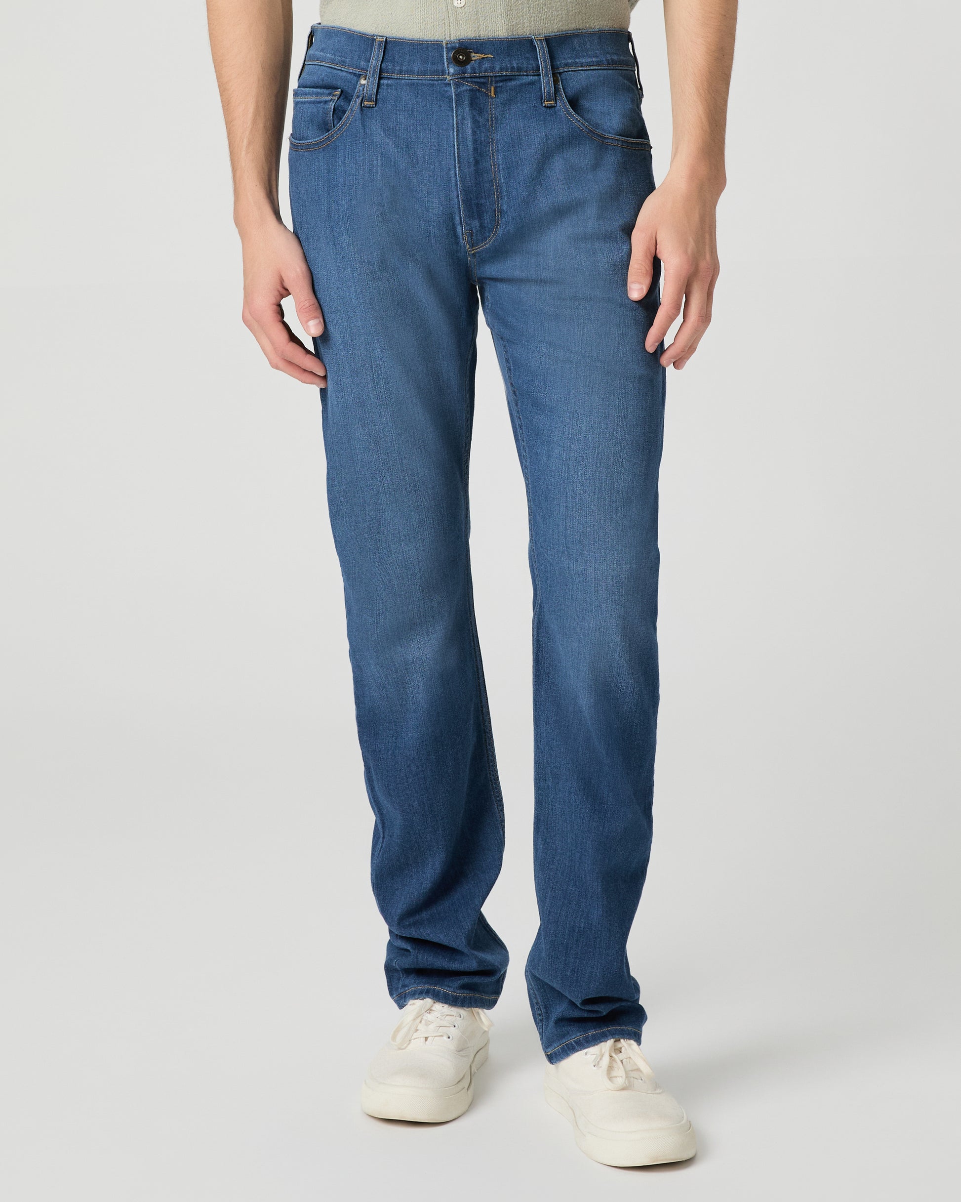 Man wearing a light green shirt and blue jeans on a white background