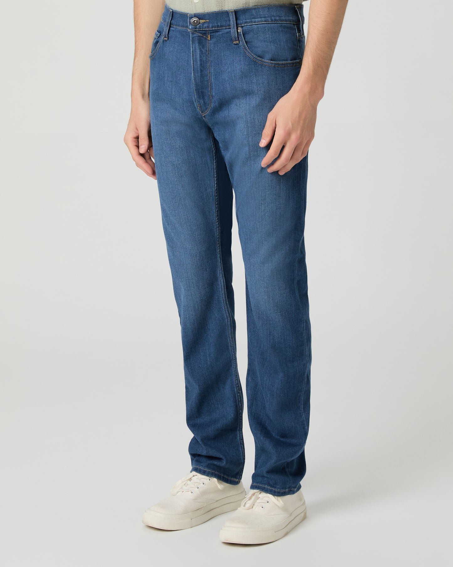 Man wearing a light green shirt and blue jeans on a white background