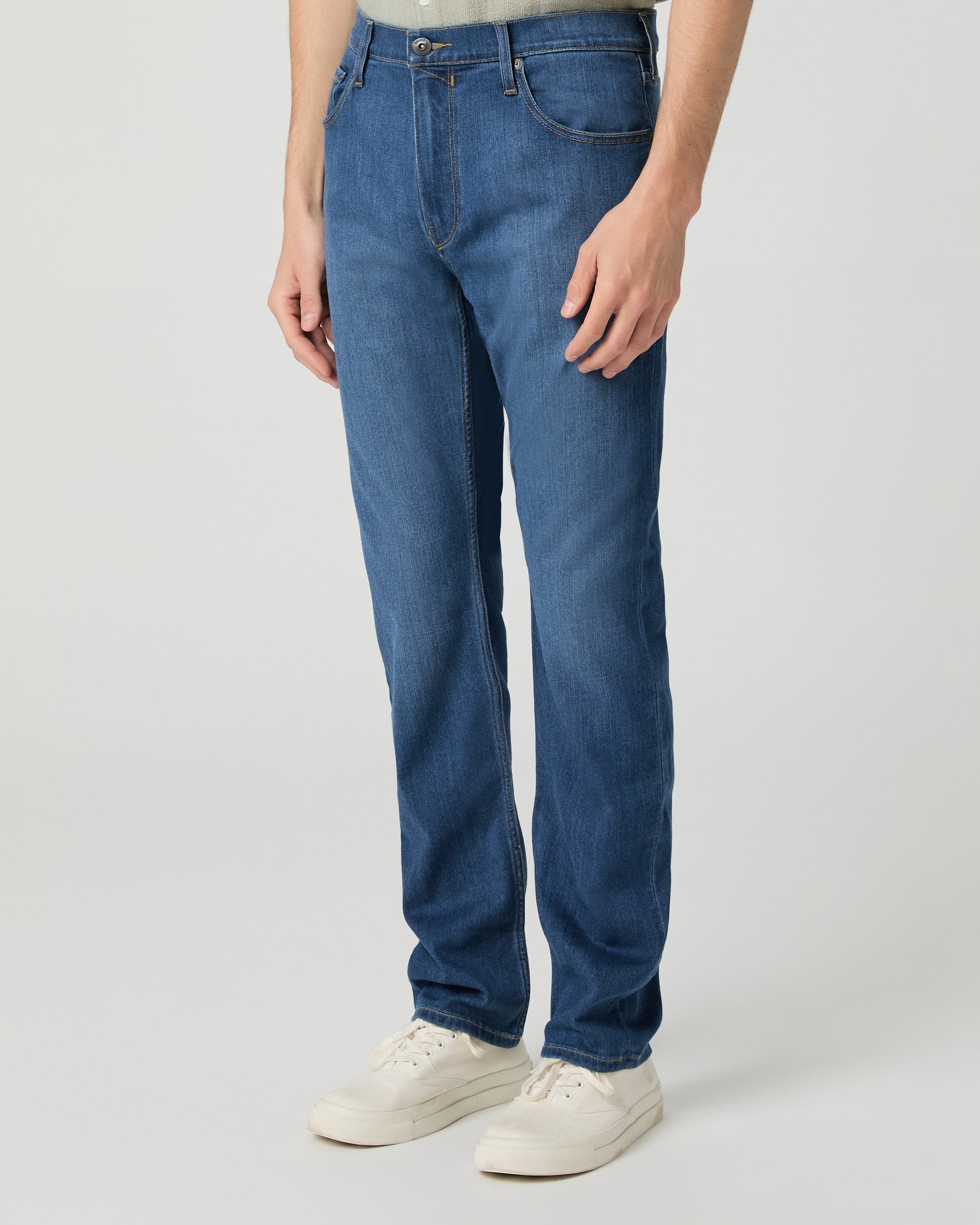Man wearing a light green shirt and blue jeans on a white background