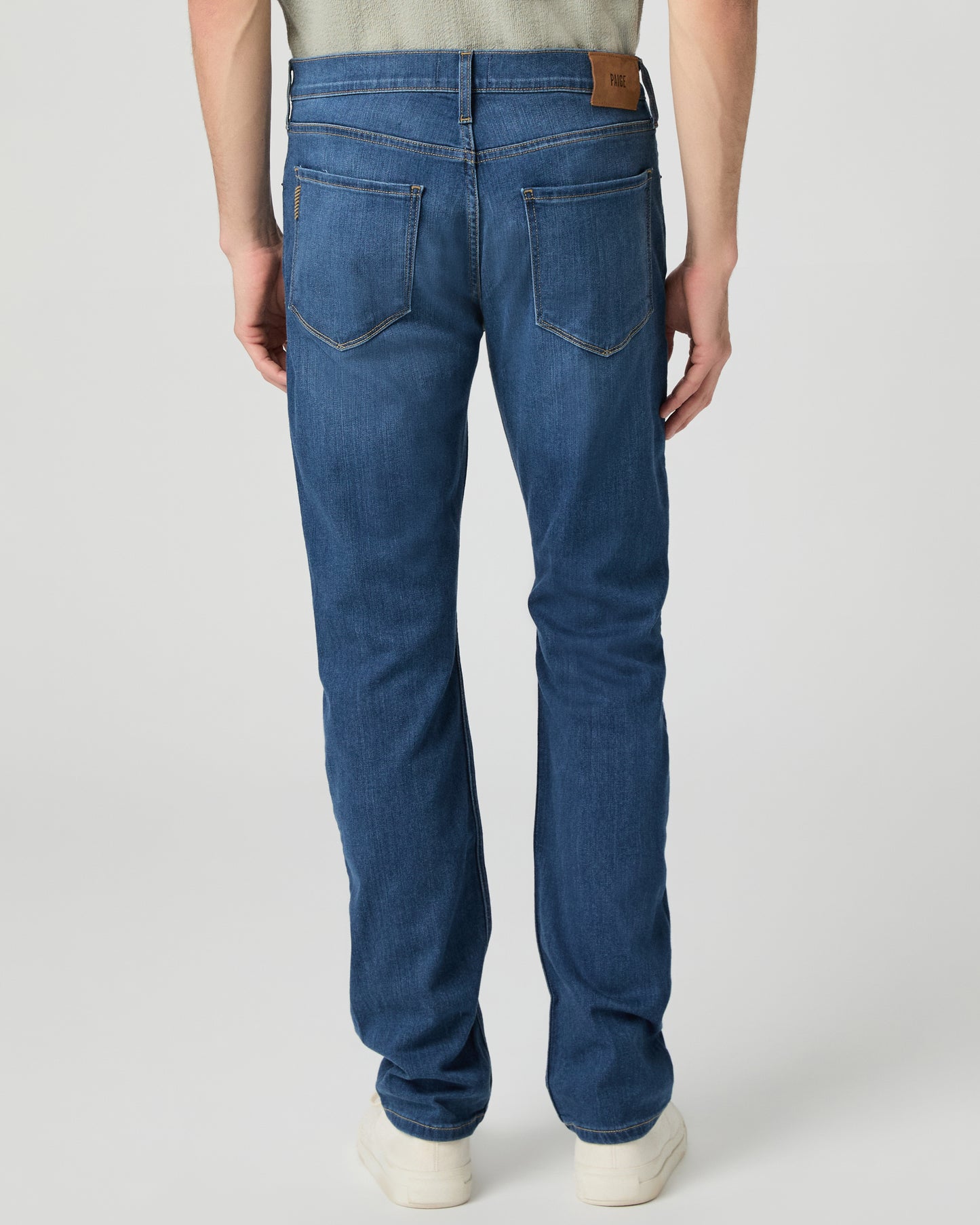 Man wearing a light green shirt and blue jeans on a white background