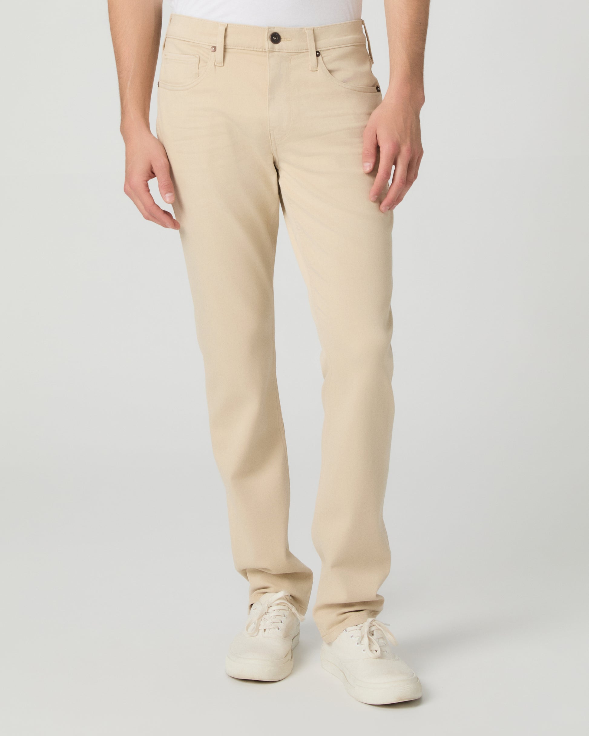 Man wearing a white shirt, beige pants, and white sneakers on a light gray background