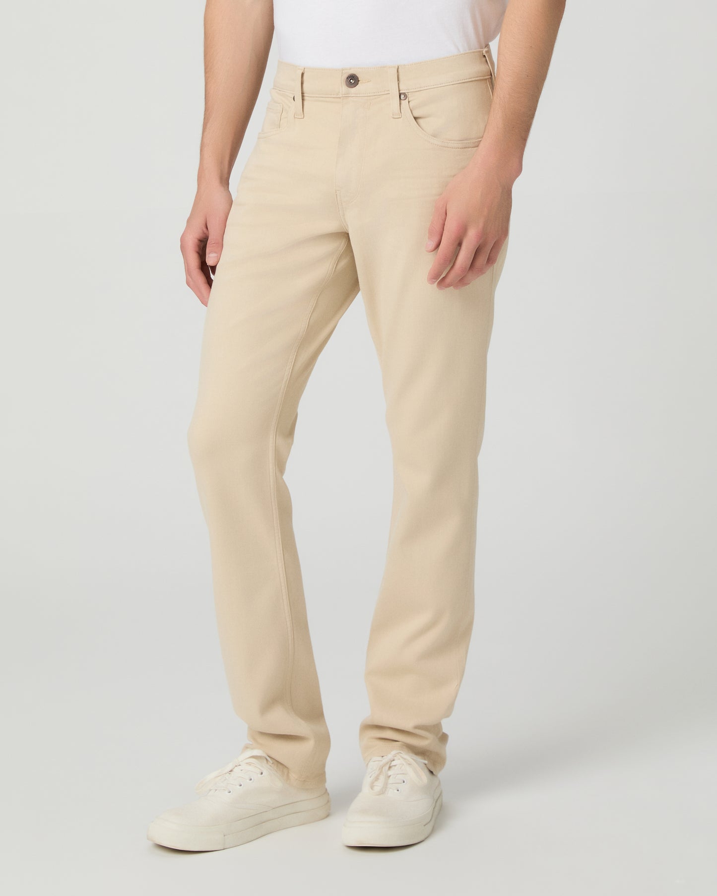 Man wearing a white shirt, beige pants, and white sneakers on a light gray background