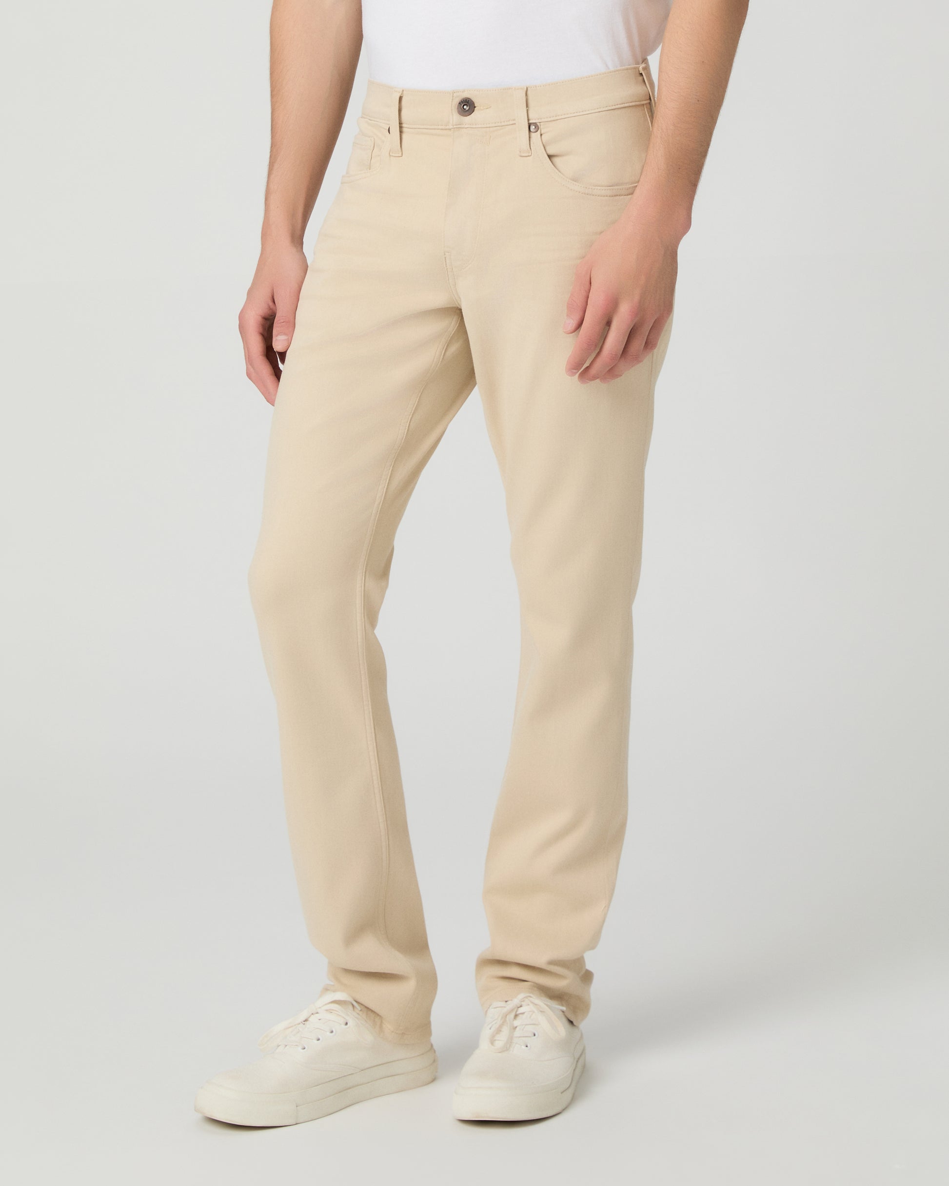 Man wearing a white shirt, beige pants, and white sneakers on a light gray background