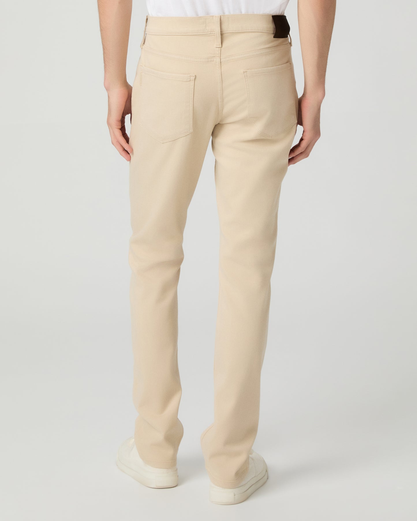 Man wearing a white shirt, beige pants, and white sneakers on a light gray background