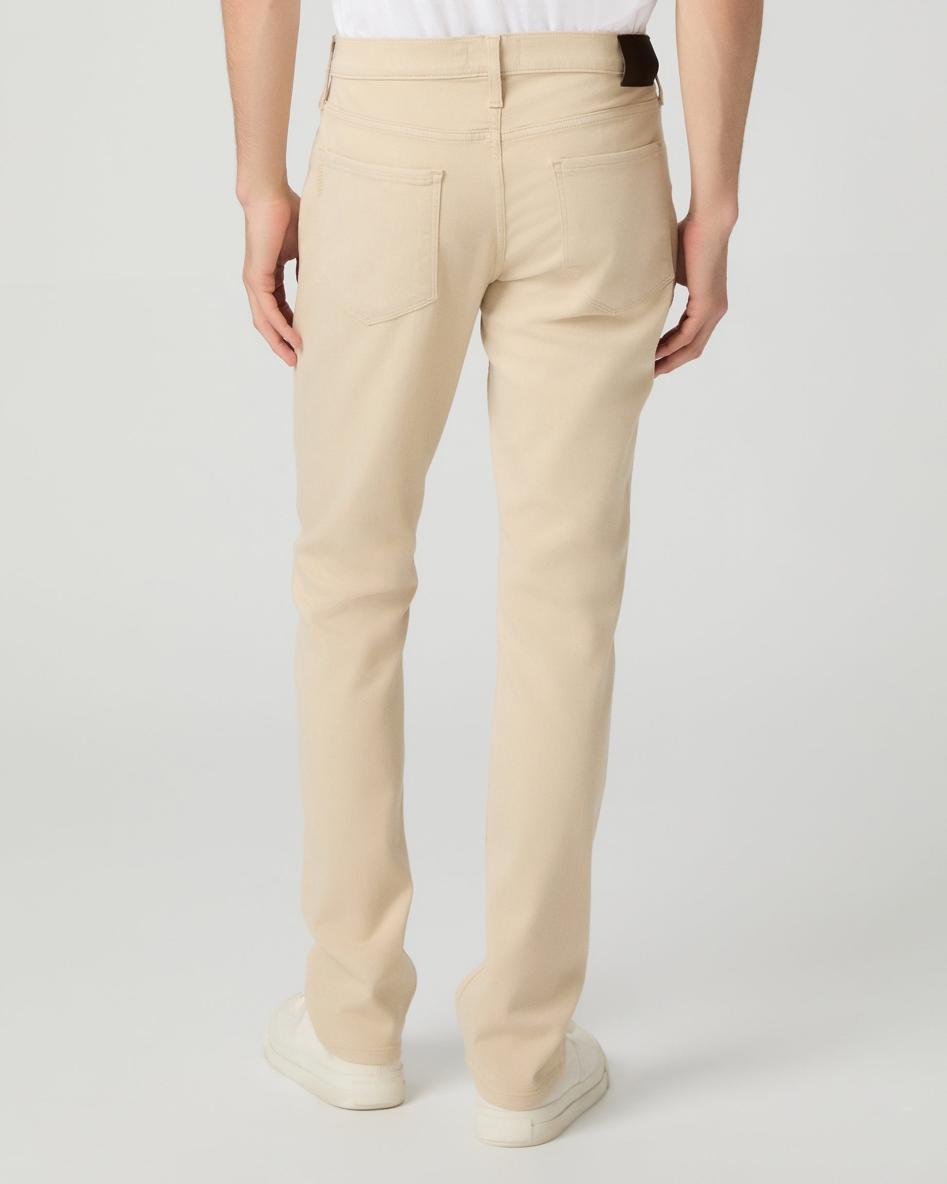 Man wearing a white shirt, beige pants, and white sneakers on a light gray background